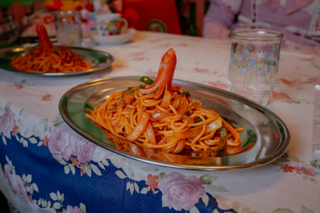 Un piatto di spaghetti Naporitan, icona della cucina yōshoku, servito su un vassoio d'argento in un kissaten. La pasta è condita con ketchup, peperoni e cipolle, guarnita con il tipico würstel a forma di polipo (tako-san wiener).