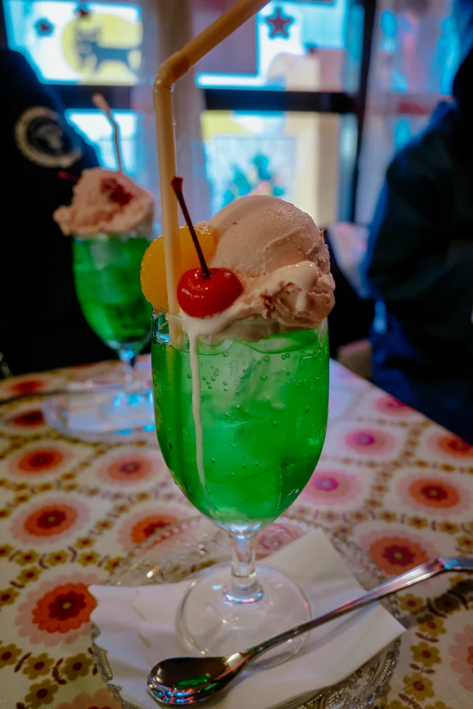 L'iconica Cream Soda al melone dal colore verde brillante, guarnita con una pallina di gelato alla vaniglia e una ciliegina sciroppata, simbolo estetico dei caffè tradizionali in Giappone.