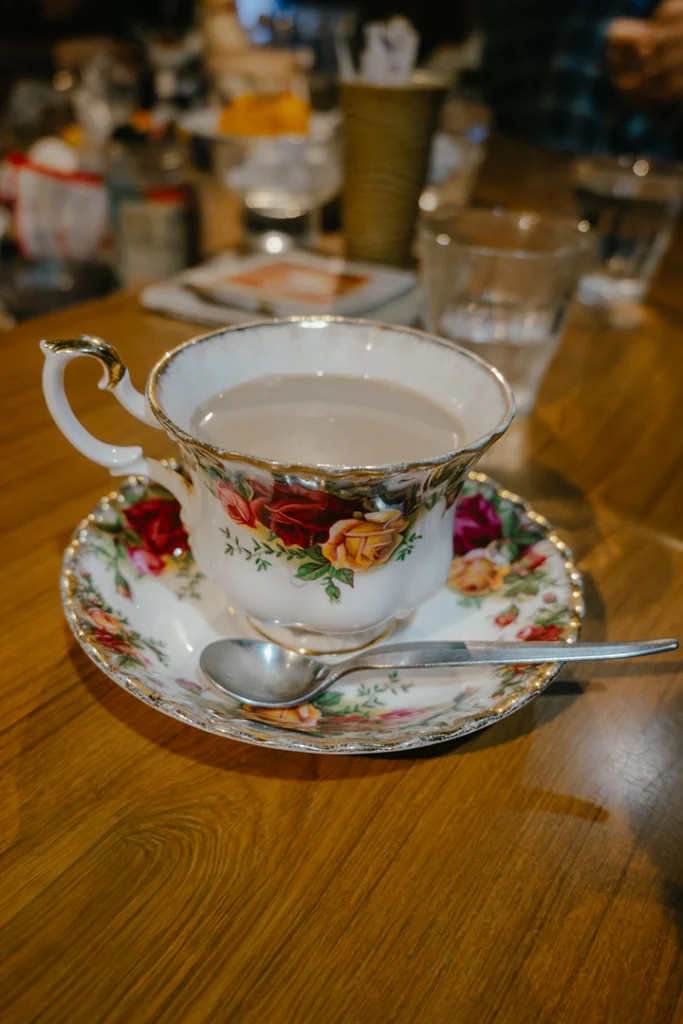 Primo piano di una tazza di caffè in porcellana pregiata decorata con motivi floreali su un tavolo di legno, simbolo della cura e del rito dei caffè tradizionali in Giappone.