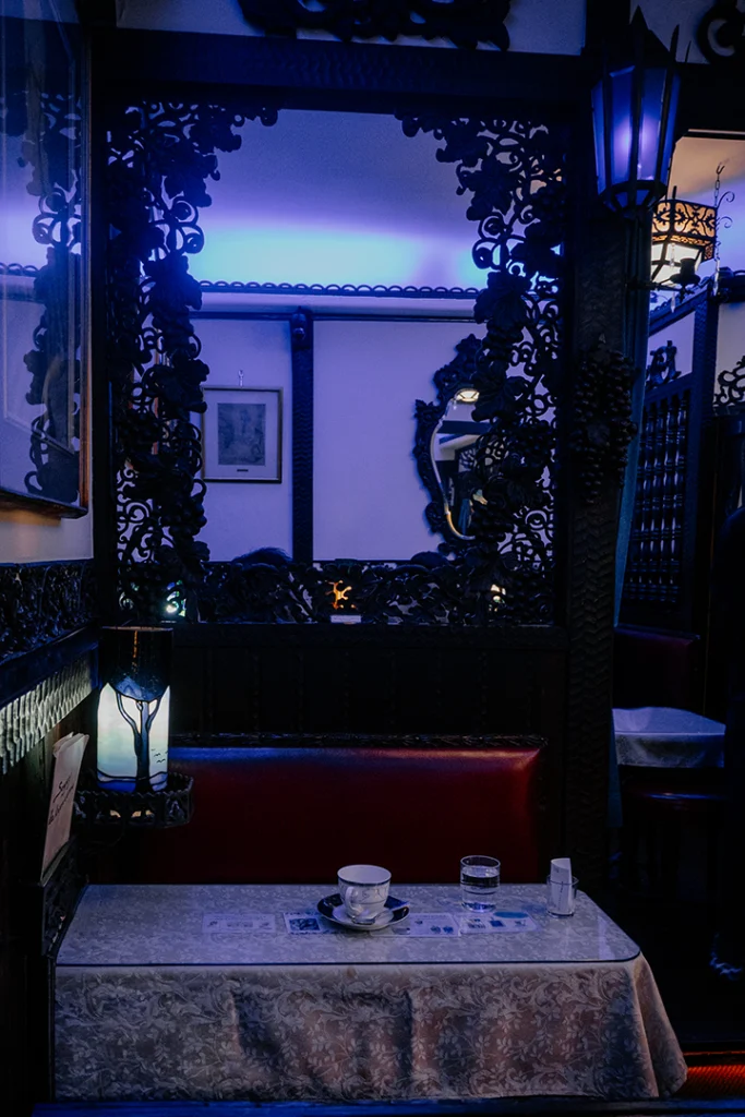 Interno del Cafè Soirée a Kyoto caratterizzato da una soffusa illuminazione blu, mobili in legno scuro intagliato e un'atmosfera d'altri tempi.