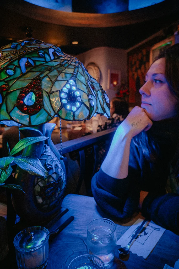 Martina di Kappamonogatari ritratta di profilo sotto una suggestiva lampada Tiffany blu all'interno del Cafè Gion ad Asagaya, Tokyo, un esempio di atmosfera jun kissaten.