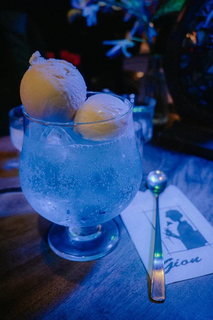 Una variante blu di Cream Soda servita in un bicchiere a calice con due palline di gelato alla vaniglia, tipica bevanda rinfrescante dell'atmosfera dei kissaten giapponesi.