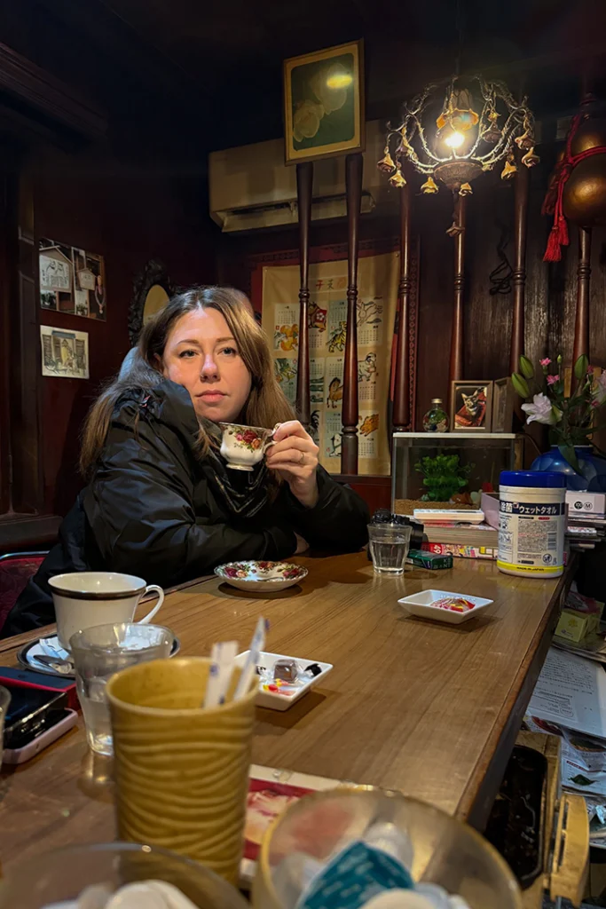 Martina di Kappamonogatari sorseggia un caffè in una tazza di porcellana decorata all'interno del Kissaten Kissa Kishi a Kanazawa, immersa nell'atmosfera calda e nostalgica dello stile Shōwa.