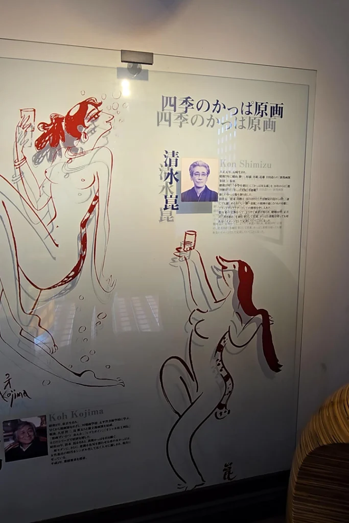 Un pannello informativo in vetro con biografie, ritratti e illustrazioni di kappa dei due famosi disegnatori giapponesi Kon Shimizu e Koh Kojima.
