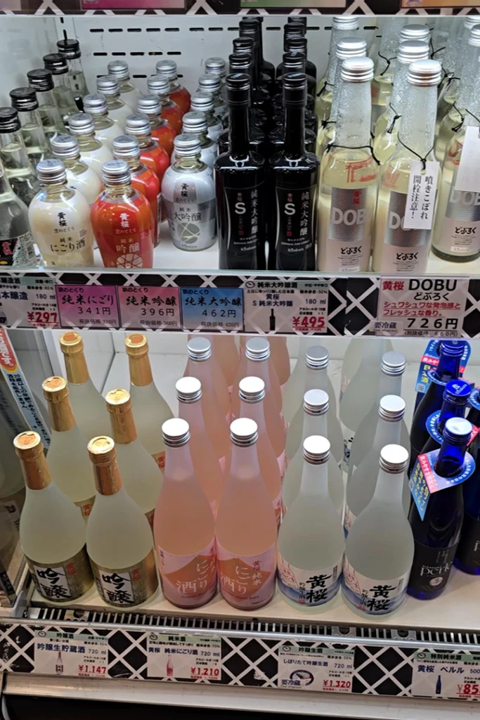 Scaffali refrigerati espositivi con varie tipologie di bottiglie di sake giapponese Kizakura, inclusi sake nigori, sake frizzante Dobu e cartellini dei prezzi in yen.