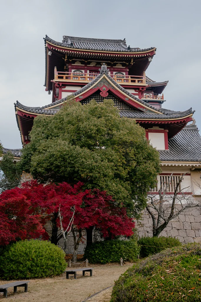 la torre minore del castello di Fushimi Momoyama a Kyoto, viste dal giardino sottostante e incorniciate da foglie di acero autunnali in primo piano.