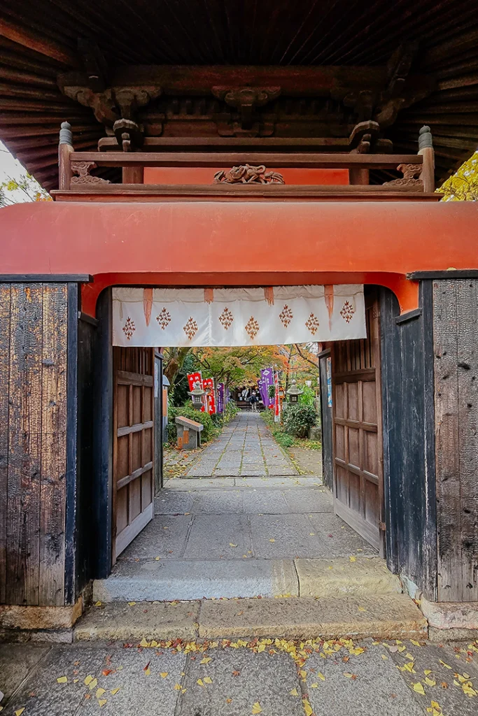 Inquadratura ravvicinata del portale del tempio Choken-ji che si affaccia sul sentiero interno in pietra, decorato con lanterne e bandiere cerimoniali colorate.